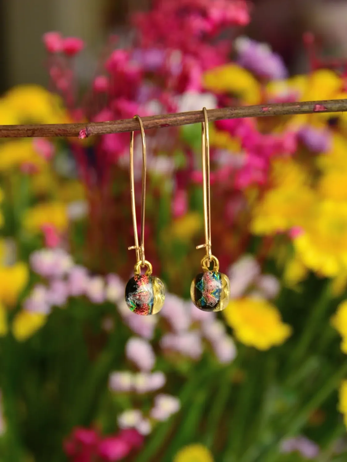 Aretes alargados con pequeñas piezas de vidrio frente a flores