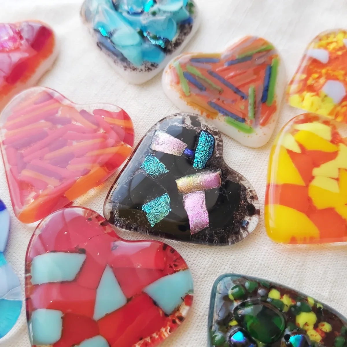 Corazones de vidrio artesanal con fragmentos de colores sobre una tela blanca